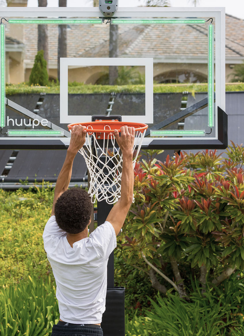 Kid dunking on the huupe ARENA in a backyard, LED backboard glowing green